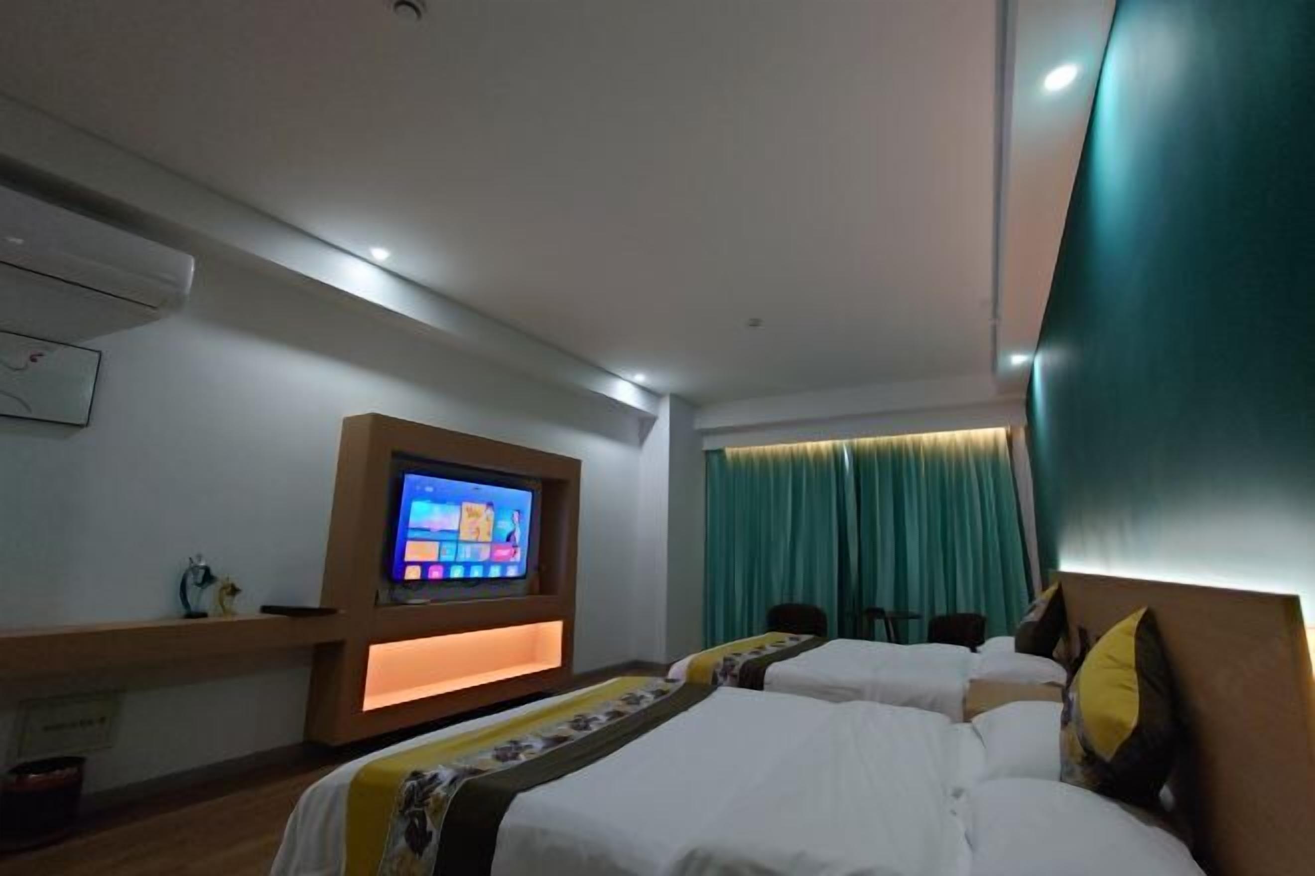 Une chambre d’hôtel avec deux lits, un téléviseur fixé au mur et une fenêtre avec des rideaux.