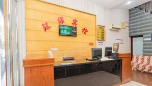 A reception desk with a wooden counter and a computer monitor. There is a television mounted on the wall above the counter. - Hengyang Environmental Protection Hotel (Hengyang)