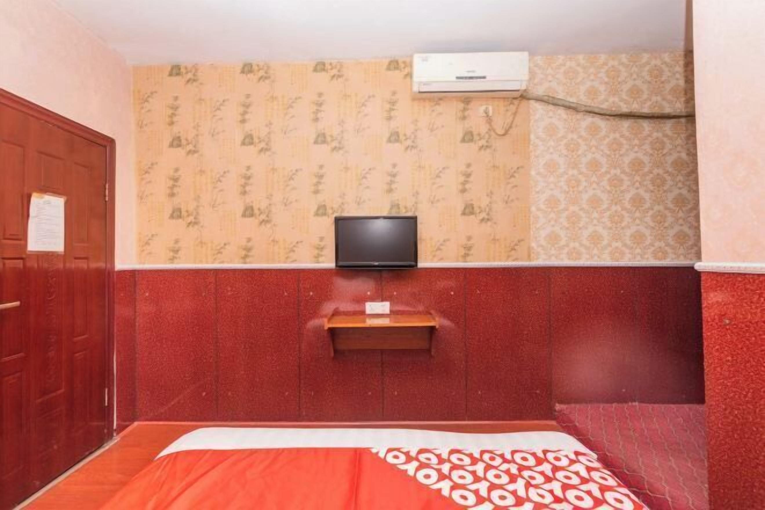 Een hotelkamer met een bed, een aan de muur bevestigde televisie, een houten plank en een airconditioner.