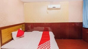A hotel room with a wooden headboard, a bed with a white and red bedspread, a wall-mounted air conditioning unit, and a blue curtain. - Hengyang Environmental Protection Hotel (Hengyang)