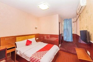 Una habitación de hotel con cama, mesita de noche, televisión y ventana con cortinas.