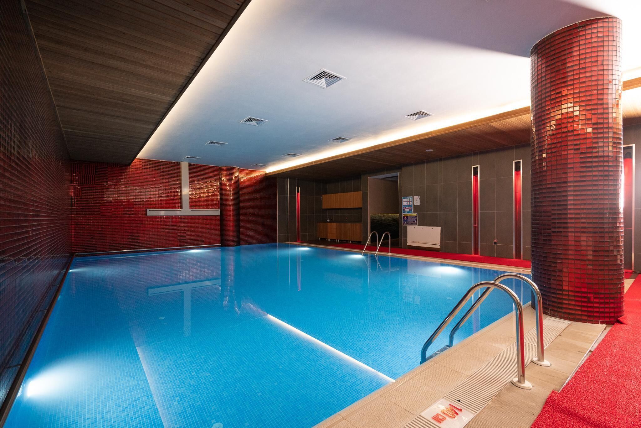 Una piscina con agua cristalina azul, rodeada de paredes de baldosas rojas y techo de madera.