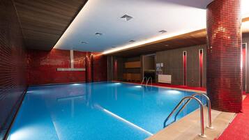 Una piscina con agua cristalina azul, rodeada de paredes de baldosas rojas y techo de madera.