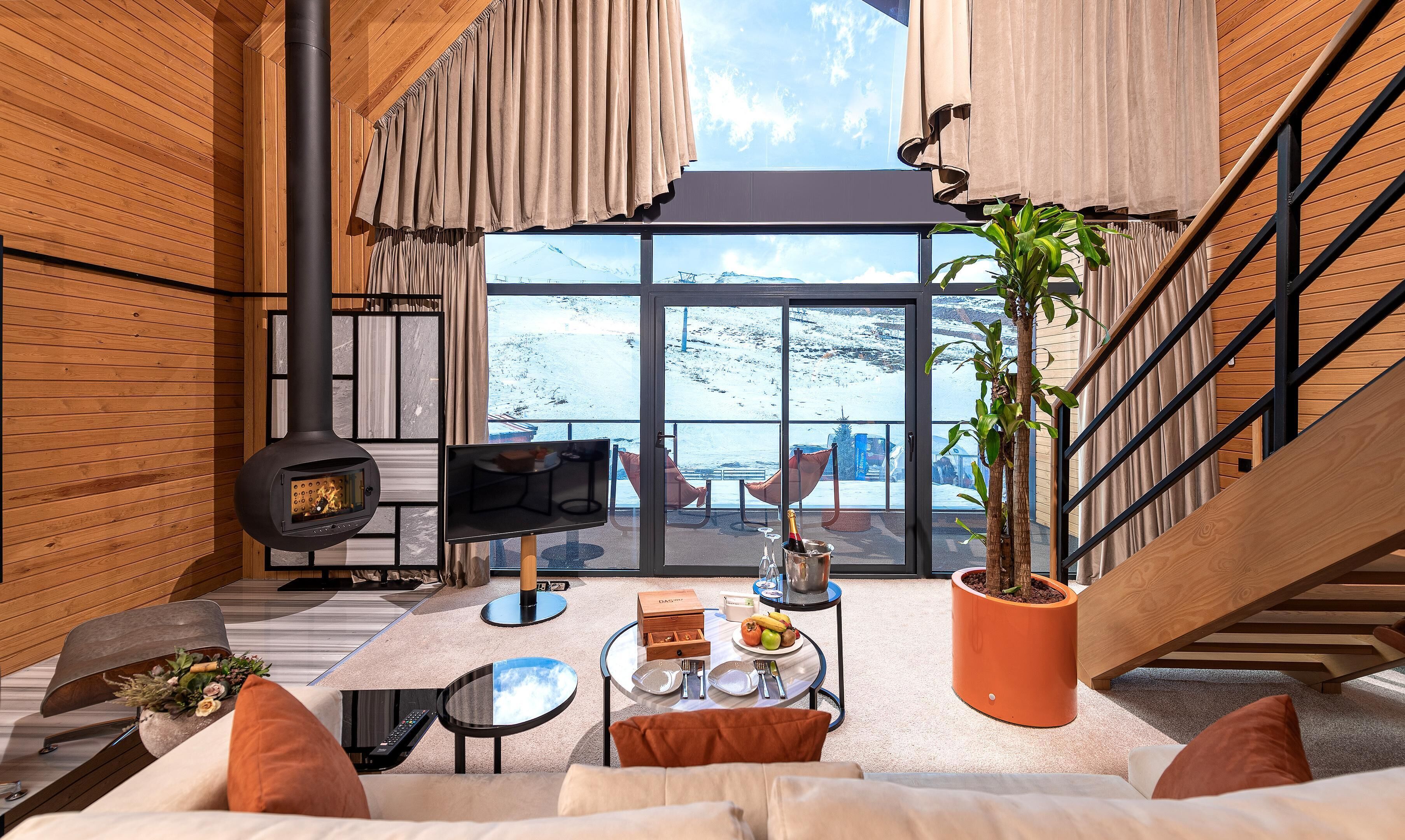 Un interior moderno con chimenea, un ventanal con vistas nevadas, una zona de comedor y una escalera.