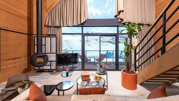 Un interior moderno con chimenea, un ventanal con vistas nevadas, una zona de comedor y una escalera.