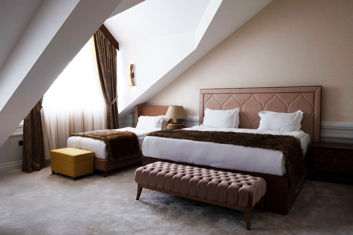 A bedroom with a large bed, a smaller bed, a bench, and a nightstand.