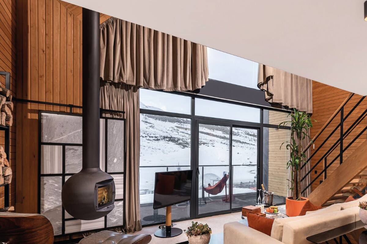 A modern living room with a large window, a fireplace, and a staircase.
