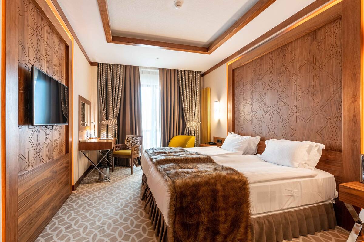 A hotel room with a large bed, a flat-screen TV mounted on the wall, a desk with a chair, and a patterned carpet.