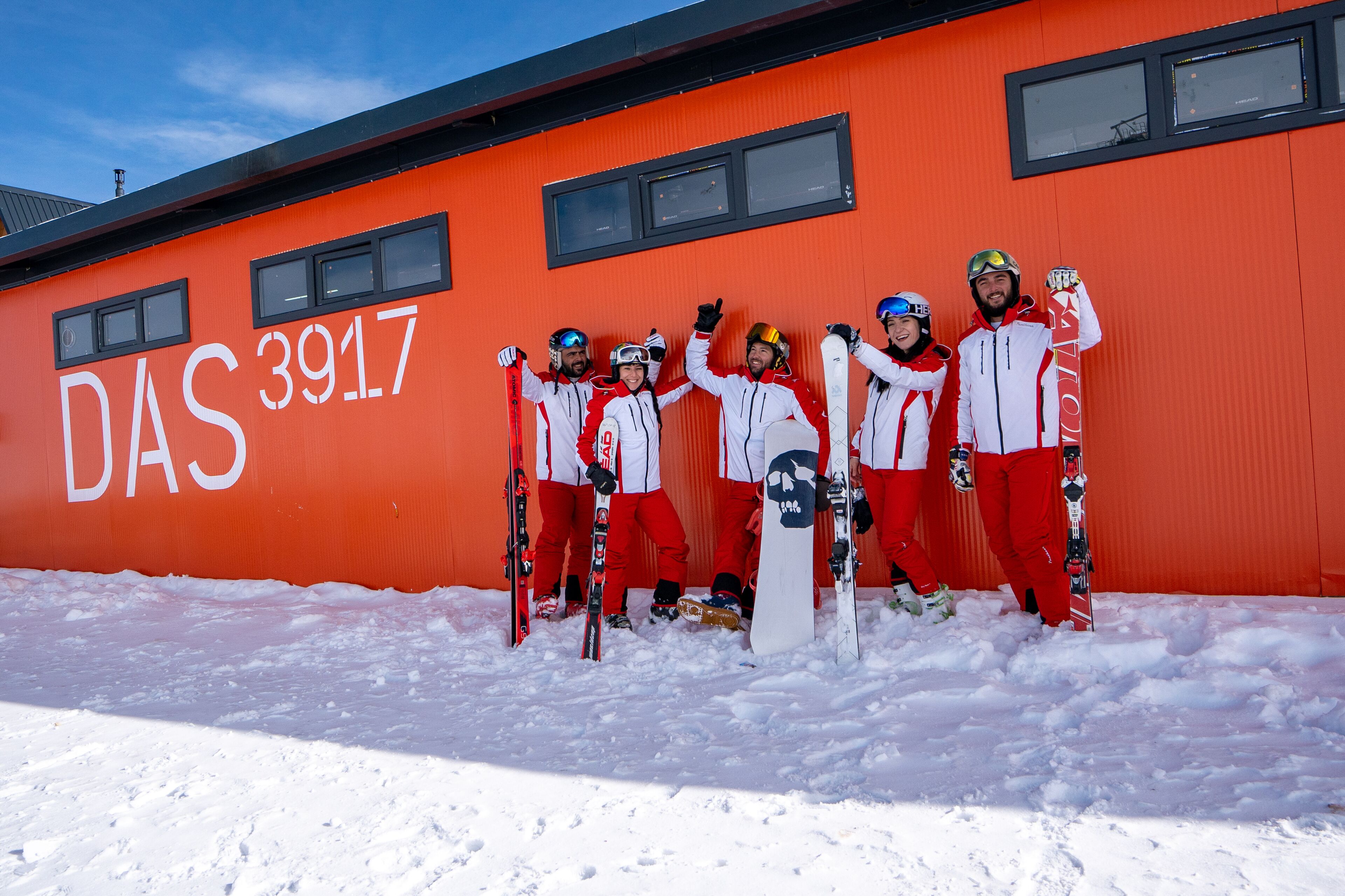 A group of skiers posing in front of a building with the text "DAS 3917".