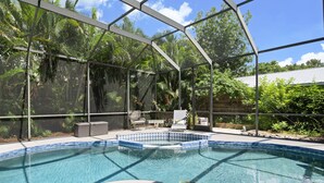 Ein Schwimmbecken mit Glasüberdachung, umgeben von üppiger Vegetation und einer Terrasse mit Sitzgelegenheiten.
