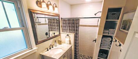 Un baño con lavamanos doble, inodoro, ducha con puerta de cristal y toallero con toallas.