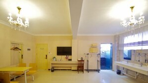 Una habitació àmplia amb una taula groga, cadires, un televisor i una finestra amb cortines.