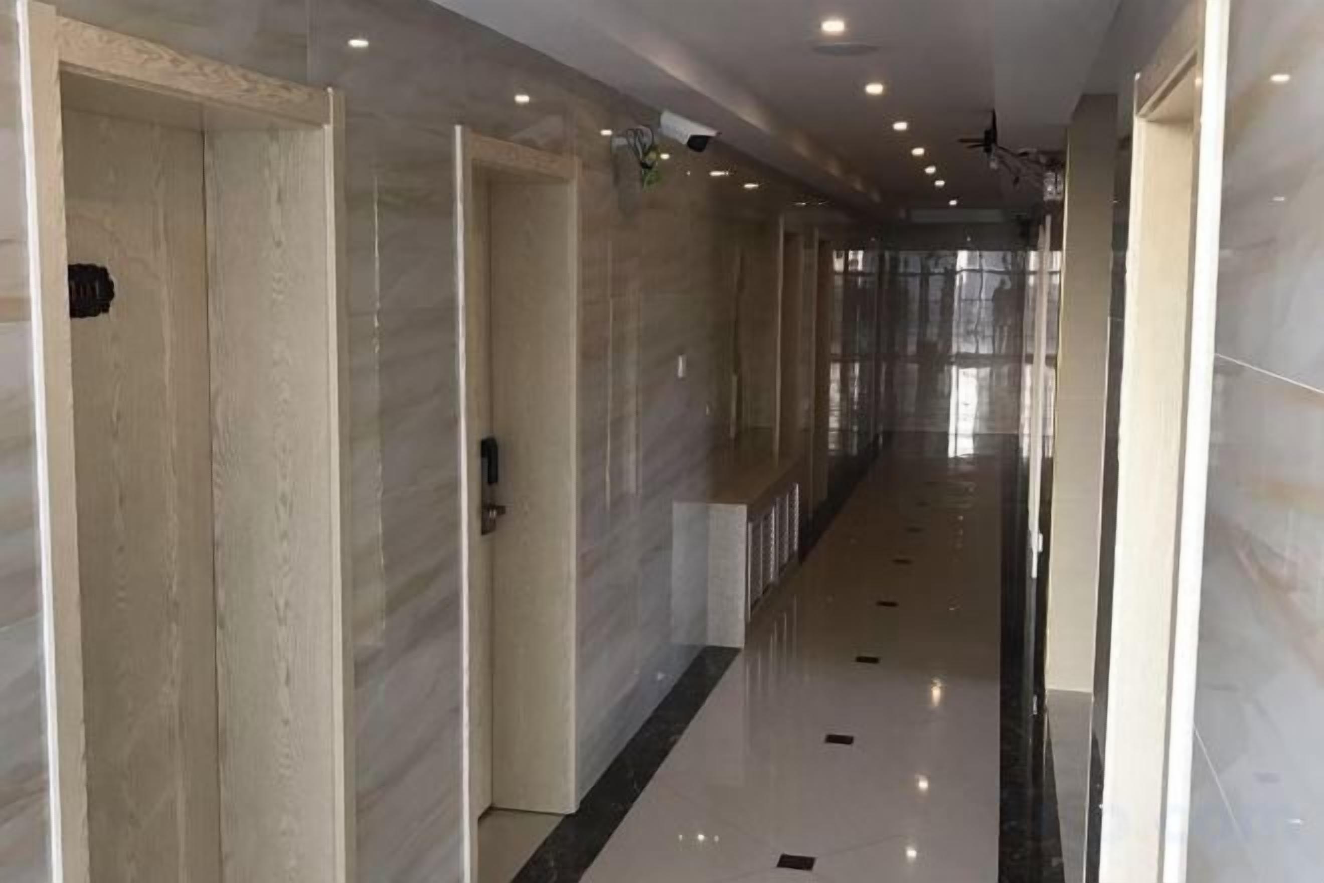 A long, narrow hallway with doors on one side and a reflective floor.