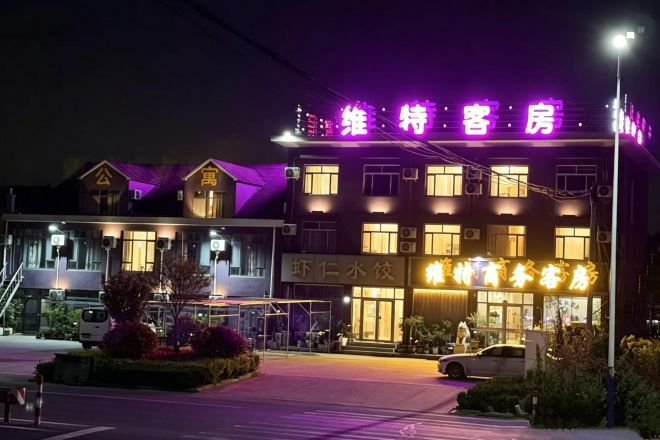 A hotel with a neon sign, a covered outdoor seating area, and a visible entrance.