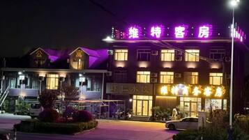 A hotel with a prominent neon sign, a parking lot, and a well-lit entrance.