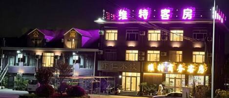 Un hôtel reconnaissable à son grand panneau lumineux, doté d’un parking et d’une entrée bien éclairée.