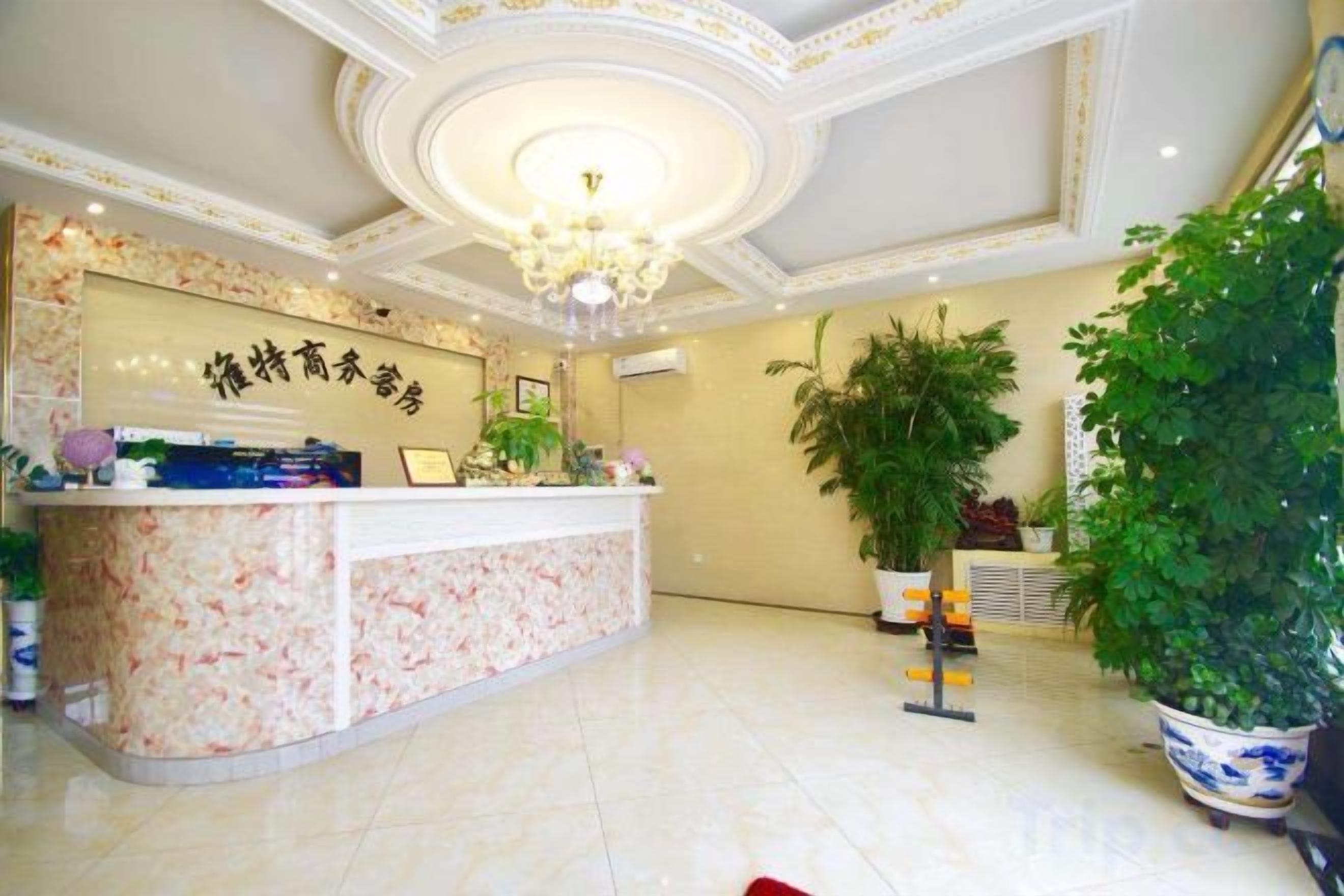 A hotel reception area with a marble counter, a chandelier, and potted plants.