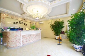 Zona de recepció d'hotel amb un mostrador de marbre, una làmpada de cristall i plantes en testos.