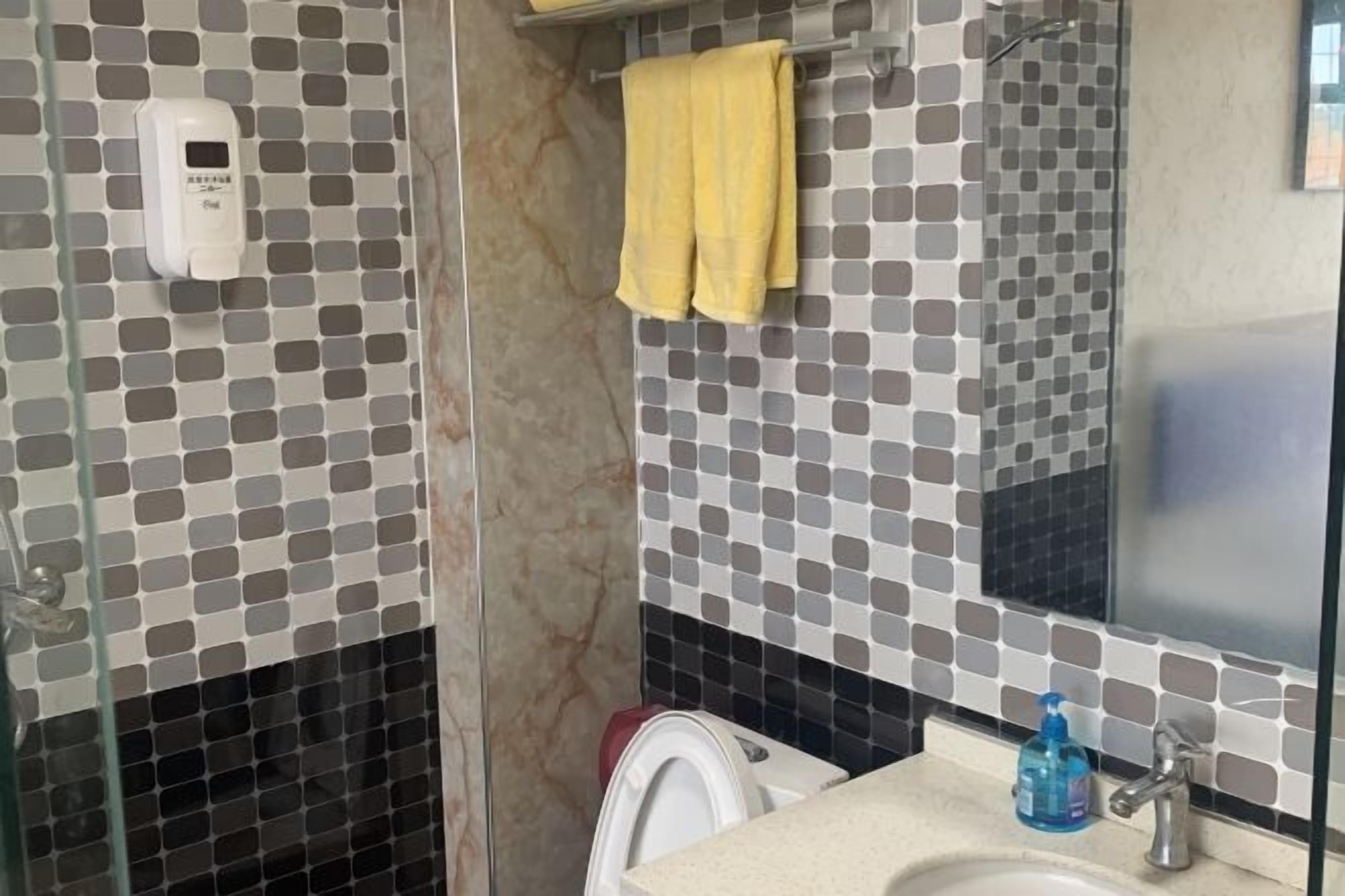 A bathroom with a tiled backsplash, a glass shower enclosure, a sink with a mirror, and a yellow towel hanging on the wall.