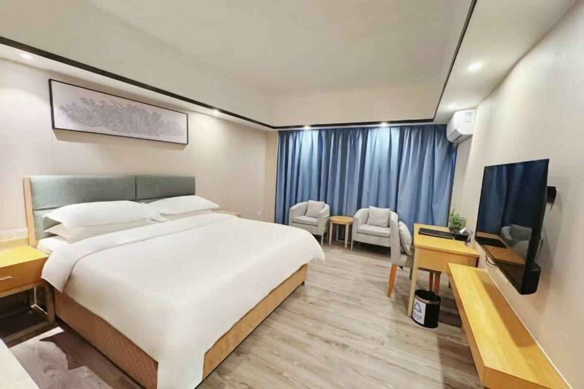 A hotel room with a large bed, a desk with a chair, a small table, and a TV.