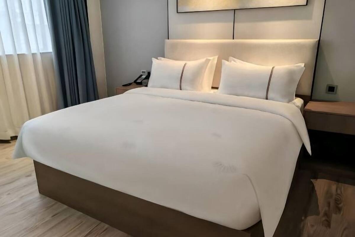 A large bed with a wooden headboard, a bedside table with a lamp, and a window with curtains.