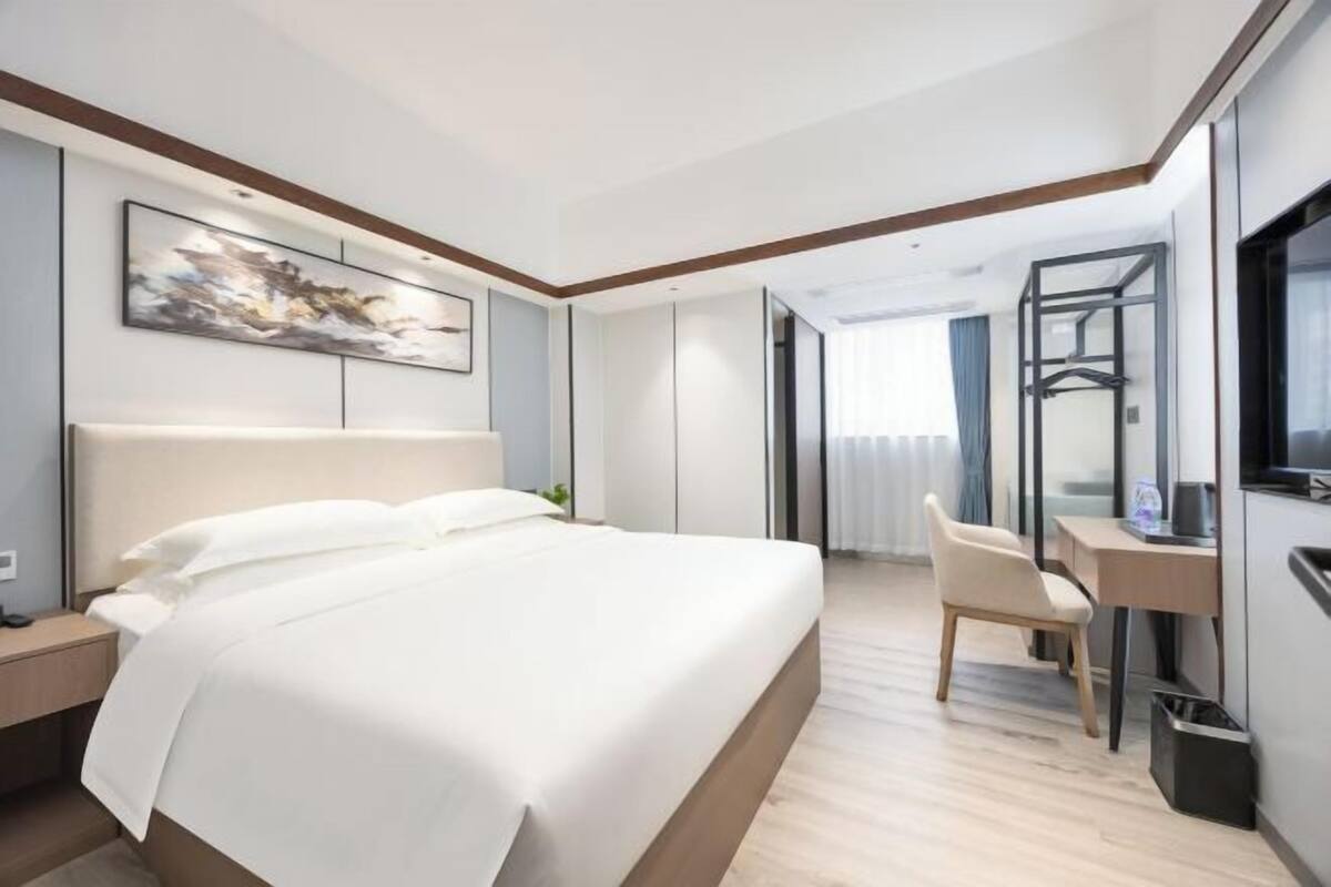 A modern hotel room with a large bed, a desk, a chair, and a mirror.