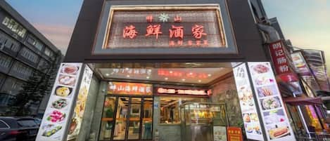 A restaurant with a prominent illuminated sign and a display of food items outside.