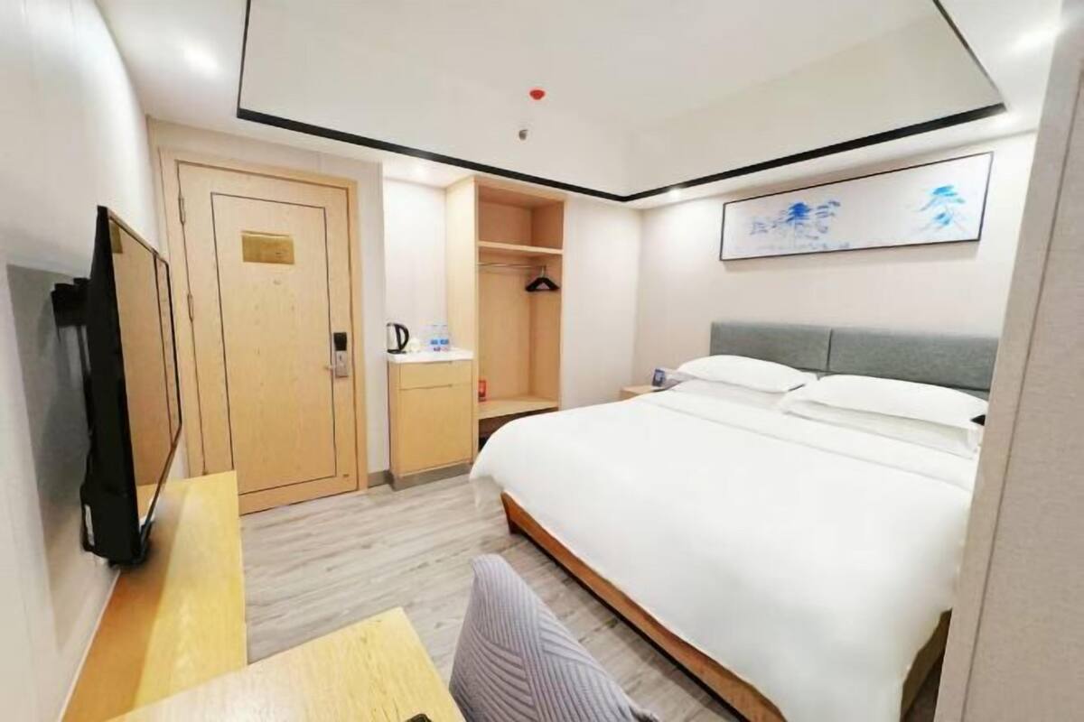 A hotel room with a bed, a desk, a wardrobe, and a mirror.