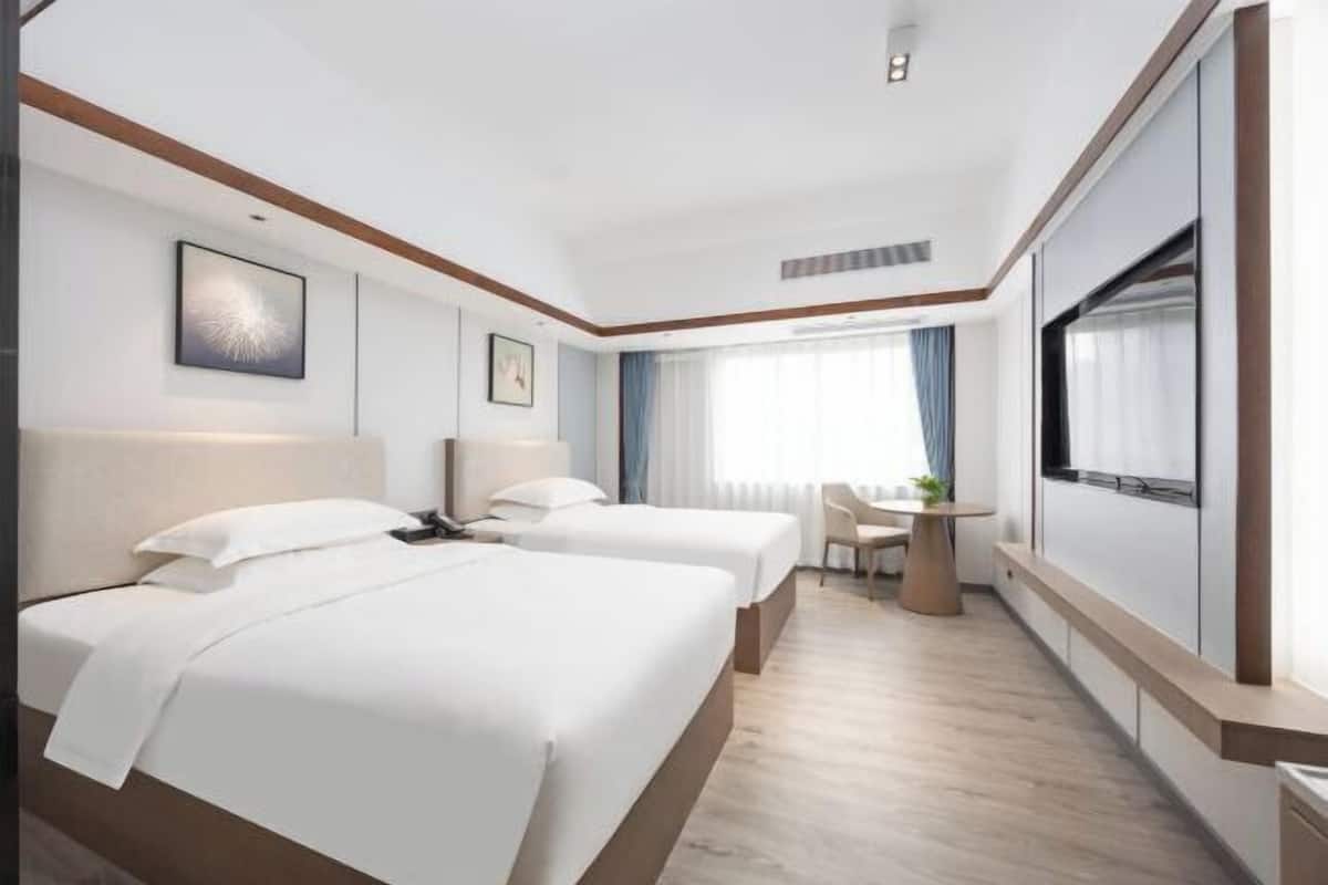 A hotel room with two beds, a desk, and a large window with curtains.