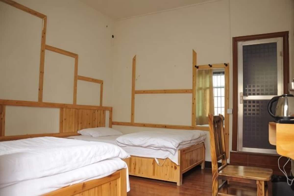 Um quarto com duas camas de madeira, uma cadeira, uma mesa e uma porta com painel de vidro jateado.