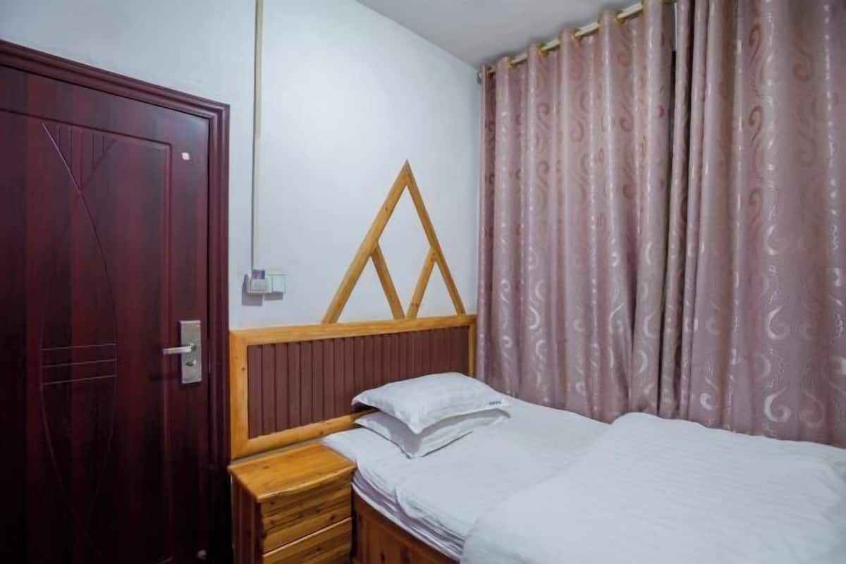 Quarto com cama de madeira, mesa de cabeceira, guarda-roupa de madeira e janela com cortinas.