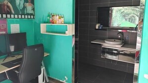 A room with a teal wall, a black tiled bathroom, a desk with a computer, and a shelf with toiletries. - I Do Theme Hotel (Panjin)