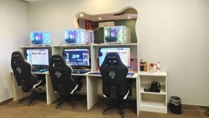 A gaming room with four gaming chairs, three gaming PCs, and a shelf with snacks. - I Do Theme Hotel (Panjin)
