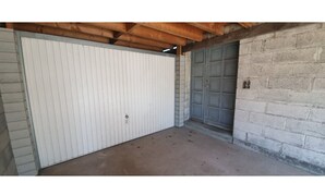 Eine Garage mit einer weißen Tür und einer grauen Tür, einem Betonboden und Holzbalkendecke.