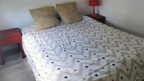 Ein Schlafzimmer mit einem Bett, einem roten Nachttisch, einer roten Lampe, einer Wandstatue Buddha und einer zierlichen Bettdecke mit geometrischem Muster.
