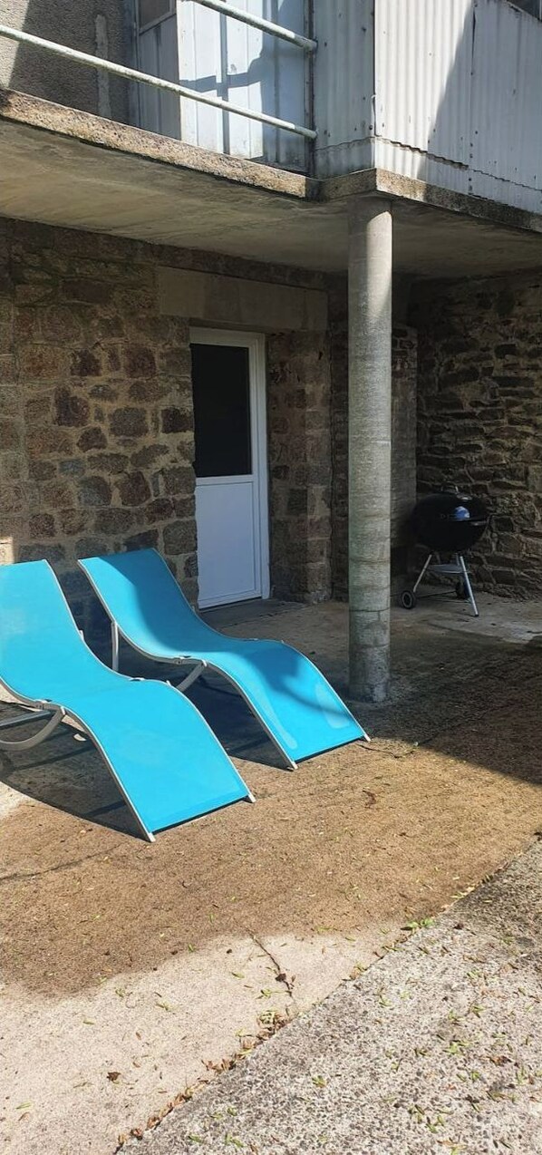Un edificio de piedra con una puerta, un pilar de concreto y dos sillones azules.