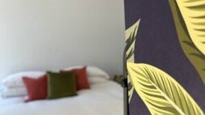 A bed with white bedding and red and green pillows, a red spherical light fixture on the wall, and a partial view of a wall with a leaf pattern. - Redwing- free parking- Grade Ii listed- ground (Huntingdon)