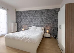 Ein modernes Schlafzimmer mit einer Wand im Steinoptik, einem großen Bett, Nachttischen mit Lampen und einem Kleiderschrank.