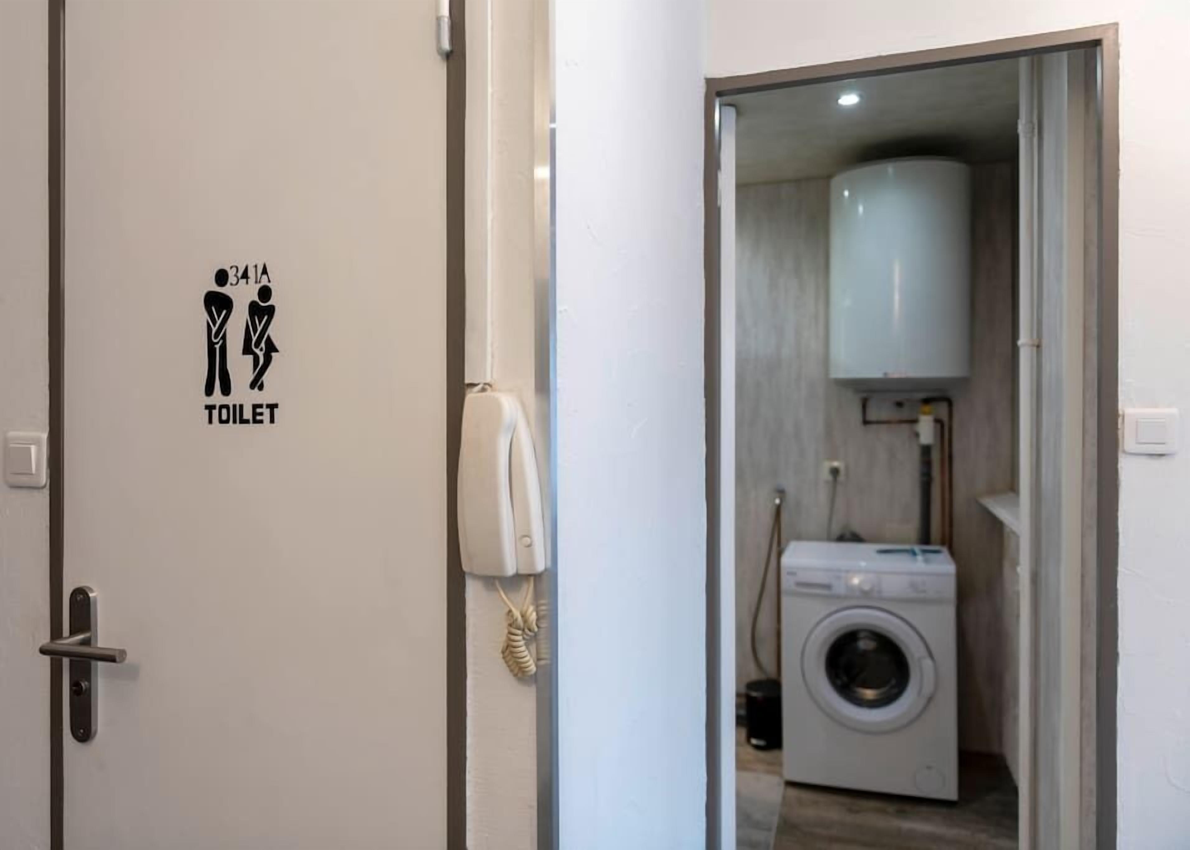 A door with a toilet sign, a phone, and a washing machine in the adjacent room.