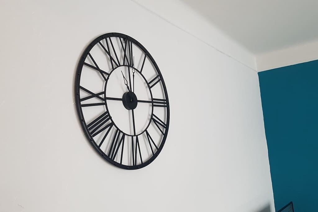 Un reloj de pared redondo con números romanos sobre una pared blanca.