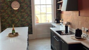 A kitchen with a large window, a clock, and a bottle of champagne on the counter. - Field Maple -free parking -Grade Ii listed- first (Huntingdon)