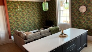 A kitchen with a central island, a sofa, and a window with a floral wallpaper. - Field Maple -free parking -Grade Ii listed- first (Huntingdon)