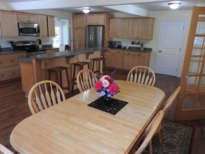 A modern kitchen with wooden cabinets, stainless steel appliances, and a dining area with a wooden table and chairs. - Coastal Charm: SW Oregon home on quiet 2+ acres, 5min. to the beach! (Gold Beach)
