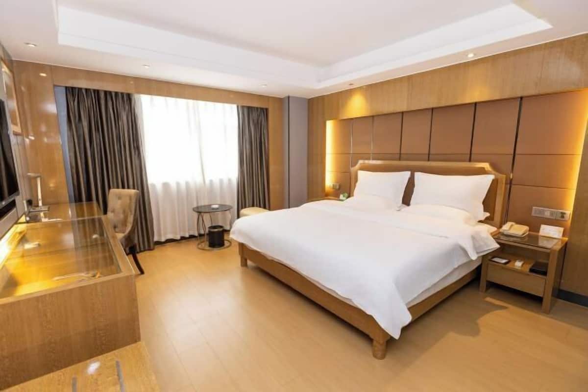 A modern hotel room with a large bed, bedside tables, a TV, and a glass-enclosed desk.