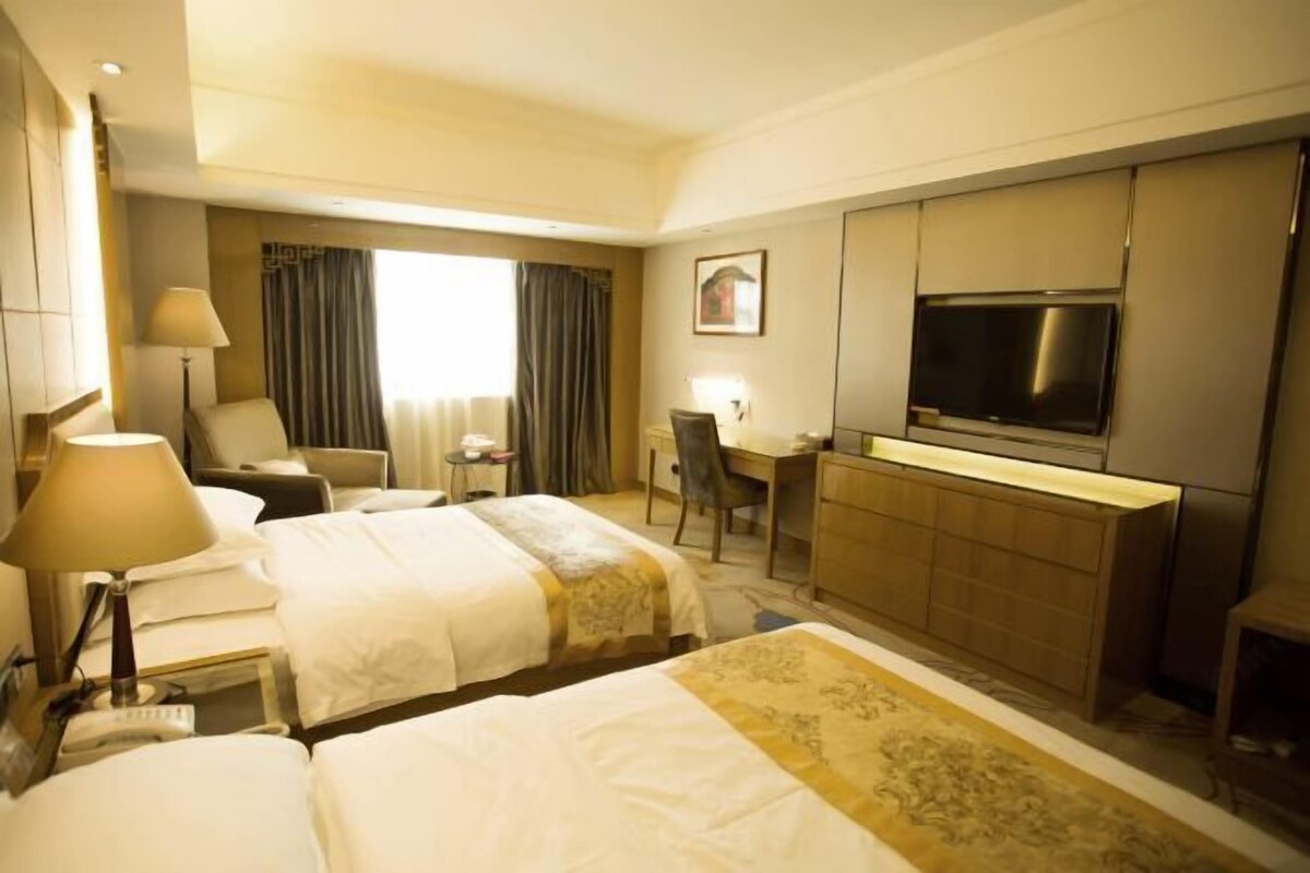 A hotel room with two beds, a desk, a TV, and a minibar.