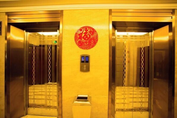 An elevator interior with a red circular emblem on the wall, a digital display, and a trash bin. - Feng Ya Hotel (Jinjiang)