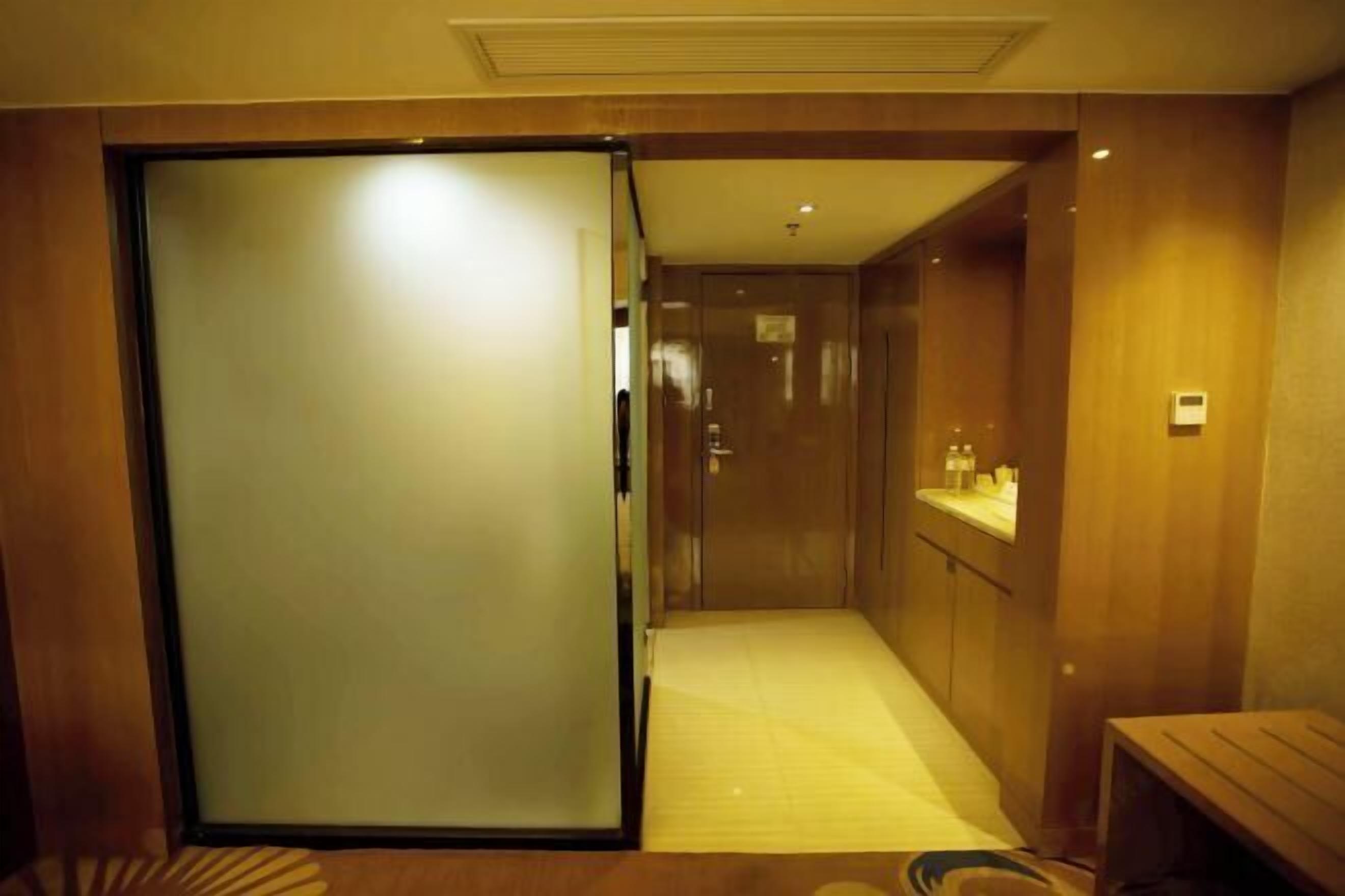 A hotel corridor with a sliding door, a small bench, and a counter with toiletries.