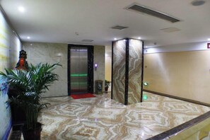 Een hotellobby met een marmeren vloer, een lift en een potplant.