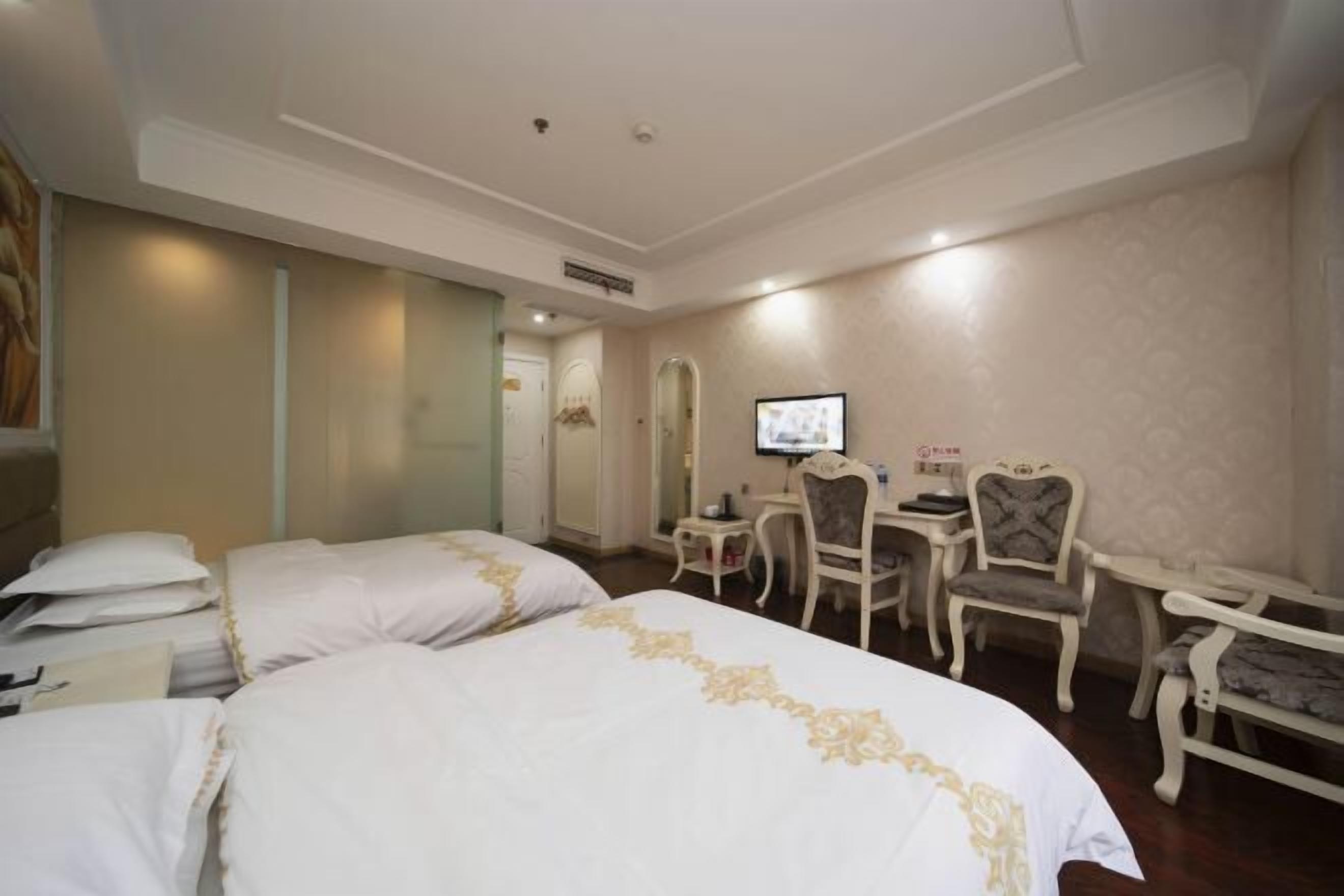 Habitación de hotel con dos camas, un escritorio, una silla y un televisor.