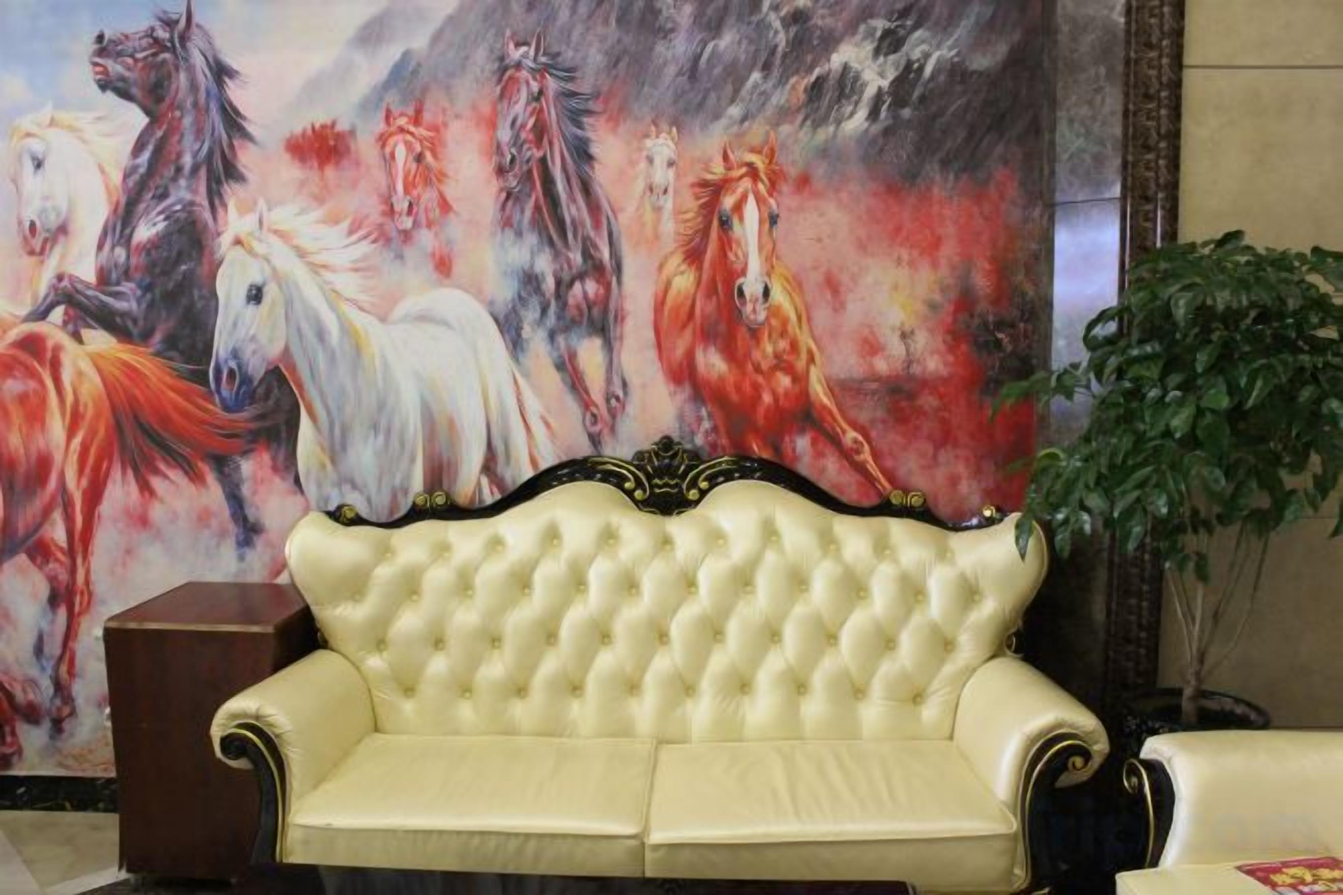 A cream-colored sofa with a tufted backrest in a room with a large horse-themed painting on the wall.